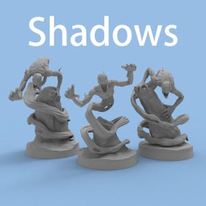 Może przedstawiać: Trzy szare miniaturowe figurki cienistych stworzeń o wydłużonych kończynach i zniekształconych cechach. Figurki stoją na okrągłych podstawach, z napisem "Shadows" w białym tekście powyżej. Tło jest jasnoniebieskie.