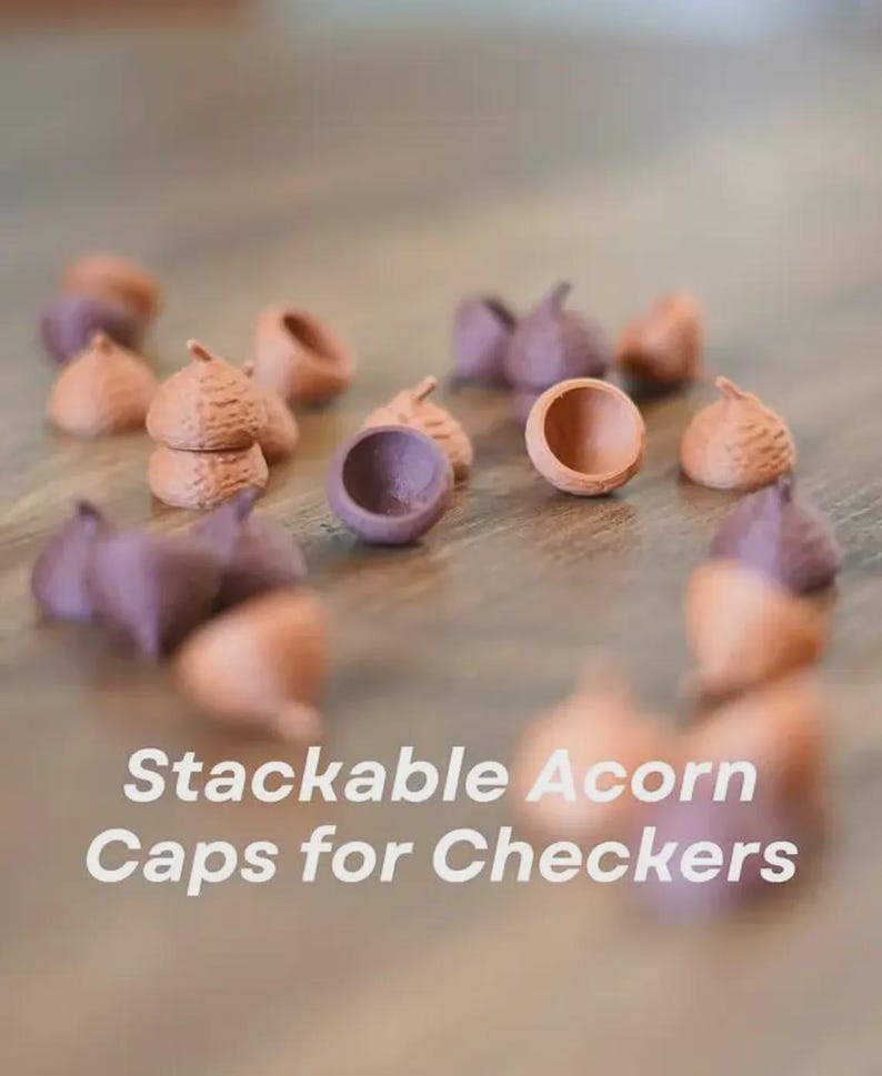 May include: A collection of stackable acorn caps in shades of brown and purple, designed for use in a checkers game. The image shows several caps scattered on a wooden surface, with the text "Stackable Acorn Caps for Checkers" in white.