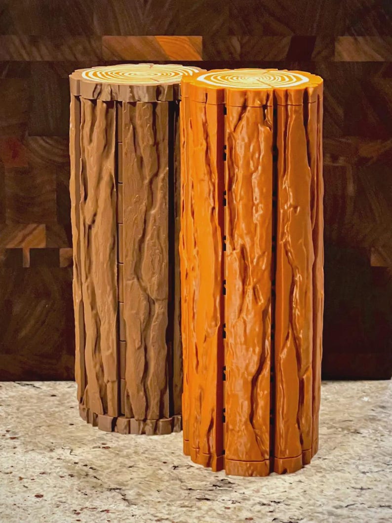 May include: Two decorative log-shaped containers. One is a light brown color, and the other is orange. Both have a textured bark design and a cross-section top with concentric circles, resembling a tree trunk. The containers are cylindrical and stand upright.