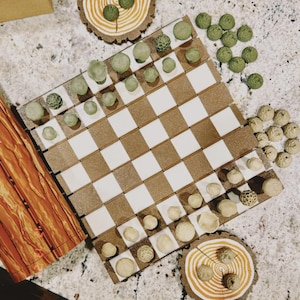 May include: A handmade chess set with a brown and white checkered board. The chess pieces are various shades of green and beige. Two decorative wooden coasters with green accents are also present.