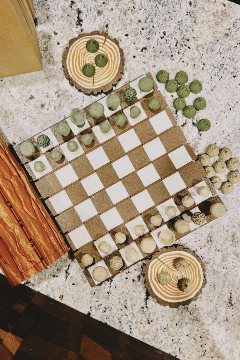 May include: A handmade chess set with a brown and white checkered board. The chess pieces are various shades of green and beige. Two decorative wooden coasters with green accents are also present.