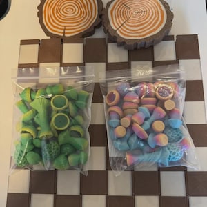 May include: A chess set with a brown and white checkered board. Two bags of colorful game pieces are visible, one green and yellow, the other a mix of pastel colors. Two wooden tree slice coasters are at the top.