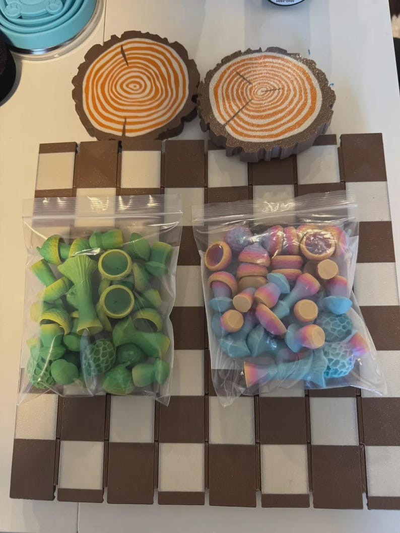 May include: A chess set with a brown and white checkered board. Two bags of colorful game pieces are visible, one green and yellow, the other a mix of pastel colors. Two wooden tree slice coasters are at the top.