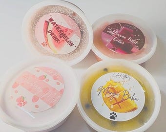 Może przedstawiać: Cztery okrągłe plastikowe pojemniki wypełnione kolorowym glutem, każdy z okrągłą etykietą. Etykiety zawierają napisy Watermelon Drink, Dragon Fruit Cubes, Strawberry Milk oraz Mango Boba, wraz z ilustracjami przedstawiającymi odpowiednie owoce.