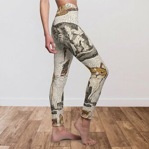 May include: High-waisted leggings featuring a mosaic-style cat design. The leggings showcase a repeating pattern of cats in various poses, with a color palette of beige, brown, and gray. The leggings are made of a stretchy material.