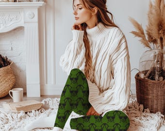 May include: Green leggings with a repeating black dog face pattern. The leggings are worn with a white cable knit sweater and white socks. The leggings are made of a soft, comfortable material.