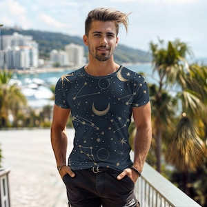 May include: Navy blue t-shirt featuring a celestial design with gold-colored stars, constellations, and crescent moons. The short-sleeved shirt has a crew neck and a fitted silhouette, perfect for casual wear.
