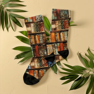 May include: Socks featuring a print of a bookshelf filled with old books. The socks have black heels and toes. Green leaves are arranged around the socks on a cream background.