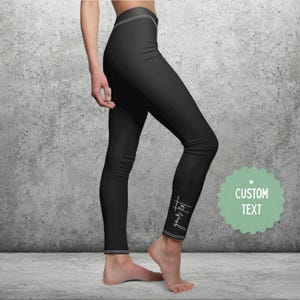 May include: Black leggings with white stitching details. The text "your text" is written in a script font on the lower leg. A green and white custom text graphic is on the right side.