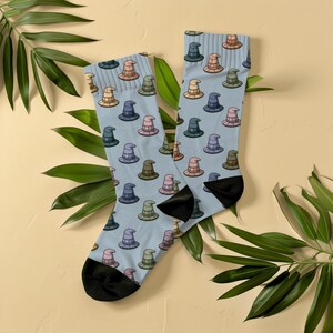 May include: A pair of light blue crew socks featuring an all-over pattern of small, pointed wizard hats in various colours including pink, green, yellow, and dark blue. The socks have solid black heels and toes, with a ribbed cuff at the top edge.