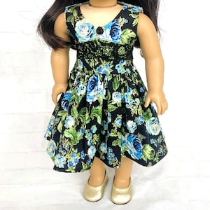 May include: A doll wearing a black floral dress with blue roses and green leaves. The dress has a V-neck, black lace detailing, and a flared skirt. The doll is also wearing gold shoes.