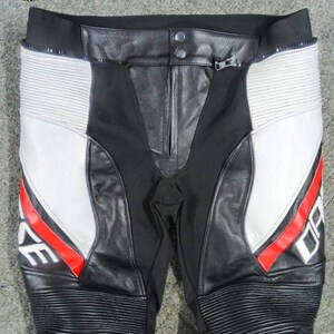 Może przedstawiać: Czarno-białe spodnie motocyklowe z czerwonymi akcentami. Spodnie posiadają sk&oacute;rzane panele, zamek błyskawiczny oraz napis "DARE" w białych literach z czerwoną obw&oacute;dką. Kolana mają żebrowany wz&oacute;r.