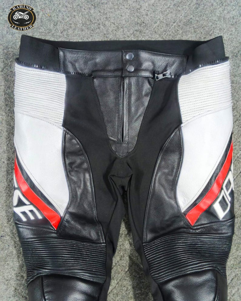 Może przedstawiać: Czarno-białe spodnie motocyklowe z czerwonymi akcentami. Spodnie posiadają sk&oacute;rzane panele, zamek błyskawiczny oraz napis "DARE" w białych literach z czerwoną obw&oacute;dką. Kolana mają żebrowany wz&oacute;r.
