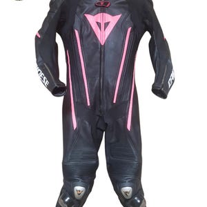 May include: Black leather motorcycle racing suit with pink detailing. Includes a full-length zip, protective padding on the knees and elbows, and the brand name "Dainese" on the sleeves. The suit is designed for speed and protection.