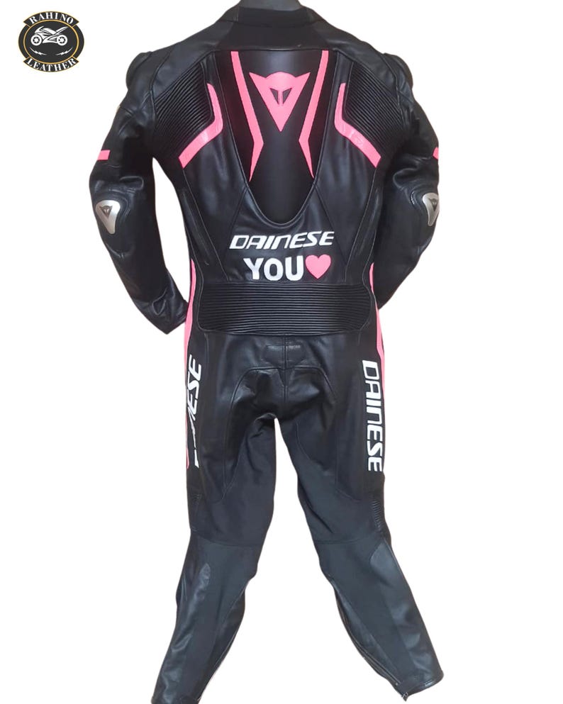May include: Black leather motorcycle suit with pink detailing and the text "DAINESE YOU". The suit features silver elbow protectors and the "RAHINO LEATHER" logo. This one-piece suit is designed for motorcycle use.