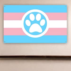 Puede incluir: Una bandera rectangular con un diseño de rayas azul claro, rosa y blanco. Un círculo blanco en el centro contiene una huella de pata azul claro. La bandera está montada en una pared.