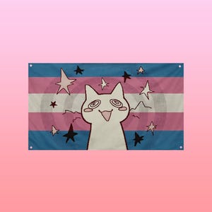 Puede incluir: Bandera rectangular con una ilustración de gato blanco, ojos arremolinados y una expresión sonriente. La bandera tiene un fondo a rayas azul, rosa y blanco con estrellas negras y blancas. El diseño incorpora los colores de la bandera del orgullo transgénero.