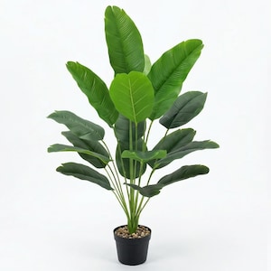 Puede incluir: Una planta artificial en maceta con hojas verdes grandes. La planta tiene un grupo de hojas anchas de color verde oscuro y hojas de color verde claro. La maceta negra está llena de pequeños guijarros. El fondo es blanco.