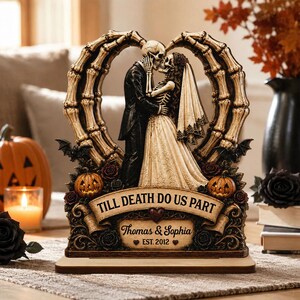 Puede incluir: Una figura decorativa de boda con esqueletos que muestra a una pareja besándose bajo un arco de huesos en forma de corazón. La base muestra el texto TILL DEATH DO US PART, Thomas & Sophia y EST. 2012, con pequeñas calabazas, rosas y murciélagos.