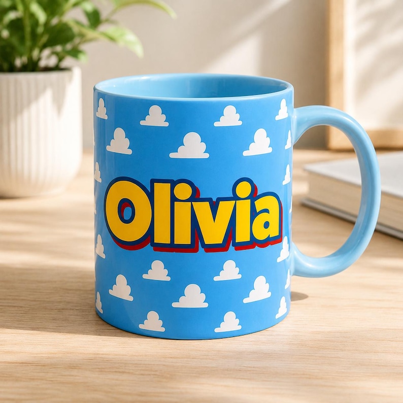 K&ouml;nnte beinhalten: Ein hellblauer Keramikbecher mit einem sich wiederholenden Muster aus kleinen wei&szlig;en Wolken. Der Name Olivia ist in gro&szlig;en, fetten gelben Buchstaben mit dunkelroter Umrandung in der Mitte des Bechers aufgedruckt, der einen passenden Henkel hat.