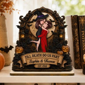 Puede incluir: Una placa decorativa con una pareja con sombrero de bruja y traje rojo abrazándose frente a una luna llena. El marco está adornado con rosas, murciélagos y calabazas. Una pancarta en la parte inferior dice TILL DEATH DO US PART, Sophia & Thomas, EST. 2012.