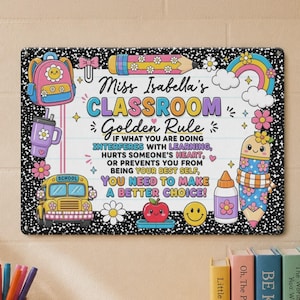 May include: A rectangular metal sign with a black and white speckled border featuring a lined paper background. It displays the text Miss Isabella's CLASSROOM Golden Rule, followed by a message about making better choices, surrounded by colorful illustrations of a backpack, pencil, rainbow, school bus, apple, and smiley face.