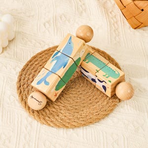May include: Wooden block puzzle featuring a blue dolphin and a green alligator. The blocks are arranged on a woven mat with wooden spheres. The puzzle is designed for children and promotes early learning.