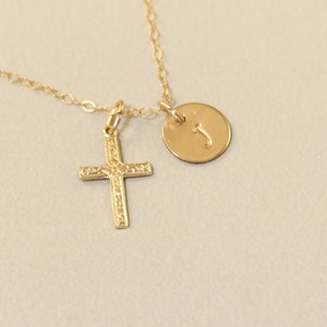 May include: A gold chain necklace with a small cross pendant and a round charm with the letter 'J' engraved on it.