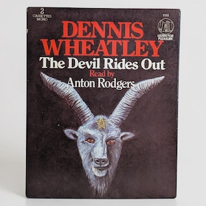 May include: A rectangular cassette tape case featuring a black background with red text reading Dennis Wheatley The Devil Rides Out Read by Anton Rodgers. The cover displays a detailed illustration of a goat head with large horns and a yellow star.