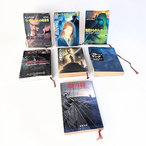 Könnte beinhalten: Eine Sammlung von sieben Taschenbüchern von A.J. Quinnell mit verschiedenen Titelbildern, darunter ein Mann, eine Frau, eine Gasmaske und ein Schiff. Jedes Buch hat ein dünnes rotes Lesebändchen, das am unteren Rand des Buchrückens befestigt ist.