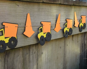 May include: A festive banner featuring orange construction cones and yellow and black dump trucks. The banner is strung on a thin twine and is perfect for a construction-themed party or event.