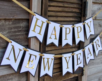 May include: A festive banner with the words "HAPPY NEW YEAR" in gold lettering on white pennants with black borders. The banner is strung with gold ribbon and is displayed against a weathered wooden background.