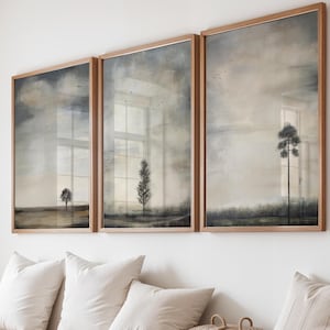 Może przedstawiać: Trzy oprawione wydruki krajobrazów w stonowanych odcieniach szarości, beżu i brązu wiszą nad drewnianą ławką z białymi poduszkami. Grafika przedstawia drzewa i zachmurzone niebo, tworząc spokojną atmosferę.