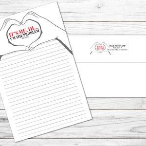 May include: A white lined stationery sheet with a heart-shaped hand design and the text "IT'S ME, HI... I'M THE PROBLEM, IT'S ME". A matching white envelope with a return address label is also included.