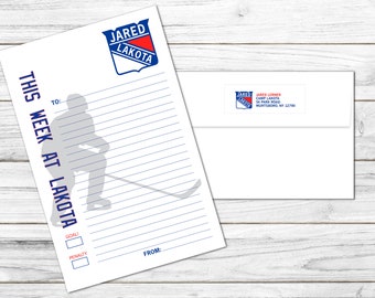 May include: A white sheet of paper with blue lines and a hockey player silhouette. The paper has the text "THIS WEEK AT LAKOTA" and a logo with the text "JARED LAKOTA". There are checkboxes labeled "GOAL" and "PENALTY".