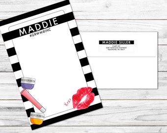 May include: A black and white striped card with the text "MADDIE #GRWM@IHC" at the top. The card has a white space for writing and a red lipstick print at the bottom. The card also has a pink lip gloss and two small jars of cream on the left side. The card is on a wooden surface. There is a white envelope with a black label that says "MADDIE SILLER CAMP INC 3287 HANCOCK HIGHWAY EQUINUNK, PA 18417" on the right side of the image.