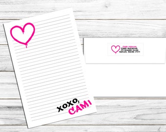 May include: A white lined paper with a pink heart and the text "XOXO, CAMI" at the bottom. A white envelope with a pink heart and the text "CAMI PARKER CAMP MATAPONI 511 SEBAGO ROAD NAPLES, MAINE 04055" is in the background.