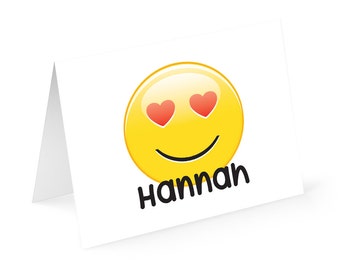 May include: Yellow smiley face with red hearts for eyes and a black smile. The text "Hannah" is below the smiley face.