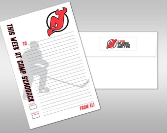 May include: A white sheet of paper with a red New Jersey Devils logo at the top. The paper has lines for writing and a silhouette of a hockey player. The text "This Week at Camp Schoodack" is written in red on the left side of the paper. The text "From Eli" is written in red at the bottom of the paper.