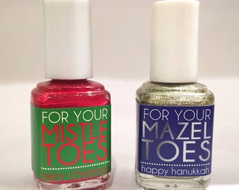 May include: Two bottles of nail polish with festive labels. The red bottle has a green label that says "For Your Mistle Toes" and "Merry Christmas". The gold bottle has a blue label that says "For Your Mazel Toes" and "Happy Hanukkah".