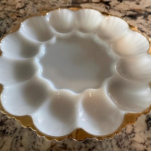 May include: A white, scalloped serving dish with a gold-colored rim. The dish has multiple compartments, perfect for serving appetizers or snacks. The dish is made of a glossy material and has a decorative, vintage aesthetic.