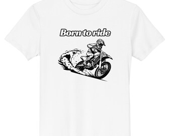 May include: A white short-sleeve t-shirt featuring a black and white graphic of a person riding a dirt bike, kicking up dust. The text "Born to ride" is printed in a bold, black font above the illustration of the motorcycle and rider.