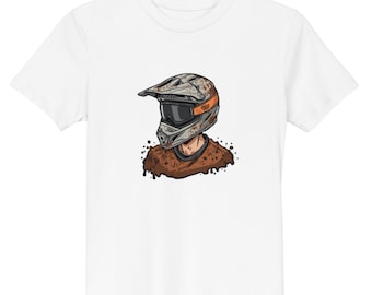 May include: A white short-sleeve t-shirt featuring a graphic illustration of a person wearing a mud-splattered motocross helmet with orange accents and dark goggles, paired with a brown shirt covered in mud splatters and drips.