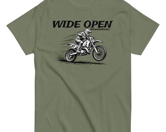May include: An olive green t-shirt featuring a black graphic of a person riding a dirt bike in mid-air. The text WIDE OPEN is printed in black above the illustration, with the word WheelieWorks printed in smaller black text to the right.