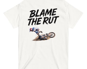 May include: A white short-sleeve t-shirt featuring the black text BLAME THE RUT printed above a graphic of a motocross rider on a dirt bike leaning into a turn on a dirt track, with the rider wearing a helmet and protective gear.