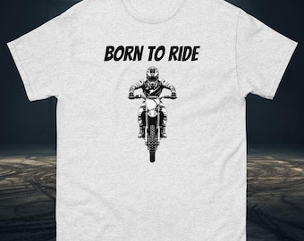 May include: A light gray t-shirt with the text "BORN TO RIDE" above a black and white graphic of a person riding a motorcycle. The rider is wearing a helmet and riding gear. The motorcycle is facing forward.