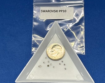 May include: A collection of small, clear Swarovski crystals, labeled "SWAROVSKI PP10", are displayed in a gray triangular tray. A U.S. dime is included for size comparison. The crystals are on a blue background.