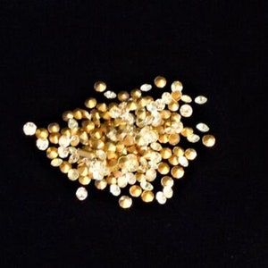 Puede incluir: Un montón de pedrería dorada y transparente sobre un fondo negro.