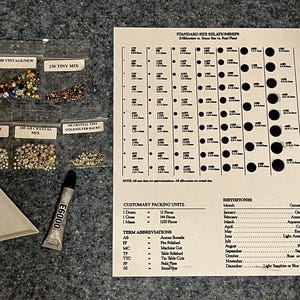 以下が含まれることがあります： ラインストーンの小袋、三角形のトレイ、E6000接着剤のチューブなど、さまざまなクラフト用品。サイズの関係と誕生石のリストが記載されたチャートも表示されています。