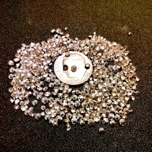 May include: A pile of small, clear, faceted rhinestones, with a silver UK fifty pence coin for scale.